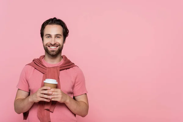 Morena hombre sosteniendo café para ir y sonriendo a la cámara aislado en rosa — Stock Photo