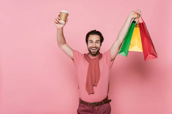 Excited man holding paper cup and shopping bags on pink background — Stock Photo