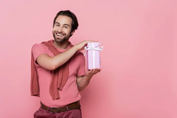 Homem sorridente segurando caixa de presente com fita isolada em rosa — Fotografia de Stock