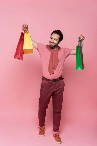 Pleine longueur de client joyeux regardant les sacs à provisions sur fond rose — Photo de stock