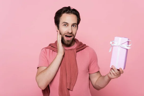 Amazed man holding gift and looking at camera isolated on pink — Stock Photo