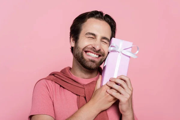 Happy man with closed eyes holding gift box isolated on pink — Stock Photo