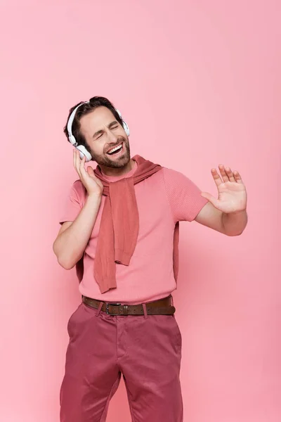 Hombre sonriente en auriculares cantando aislado en rosa - foto de stock