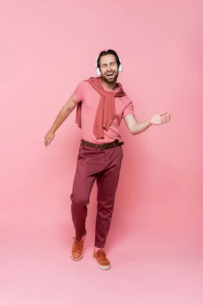 Homem com olhos fechados cantando enquanto ouve música em fones de ouvido em fundo rosa — Fotografia de Stock