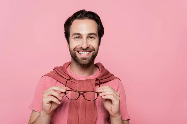 Joven sosteniendo anteojos y sonriendo a la cámara aislada en rosa - foto de stock