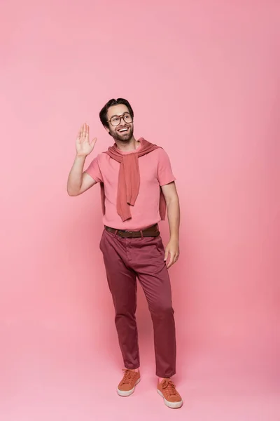 Веселий чоловік в окулярах махає рукою, стоячи на рожевому фоні — стокове фото