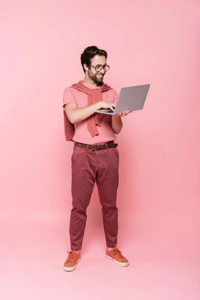 Full length of smiling freelancer using laptop on pink background — Stock Photo