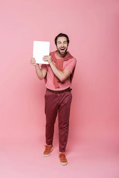 Longitud completa del hombre alegre sosteniendo el ordenador portátil sobre fondo rosa - foto de stock