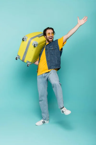 Excited tourist in sunglasses holding suitcase on blue background — Stock Photo