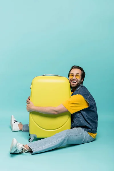Веселый мужчина обнимает чемодан на синем фоне — стоковое фото