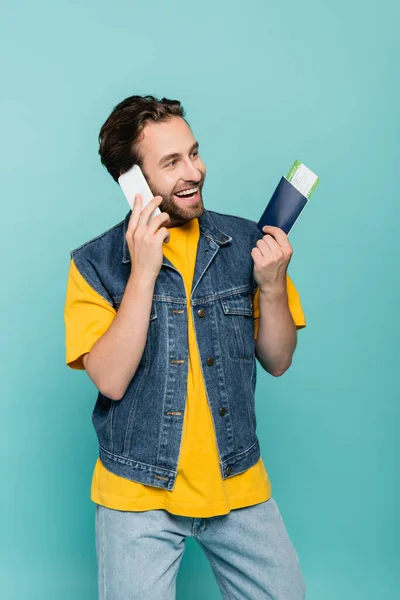 Turista alegre com passaporte falando em smartphone isolado em azul — Fotografia de Stock