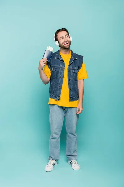 Dreamy tourist in headphones holding passport on blue background — Stock Photo