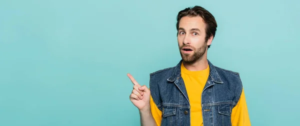 Verblüffter Mann in Jeansweste zeigt mit erhobenem Zeigefinger auf blaues Banner — Stockfoto