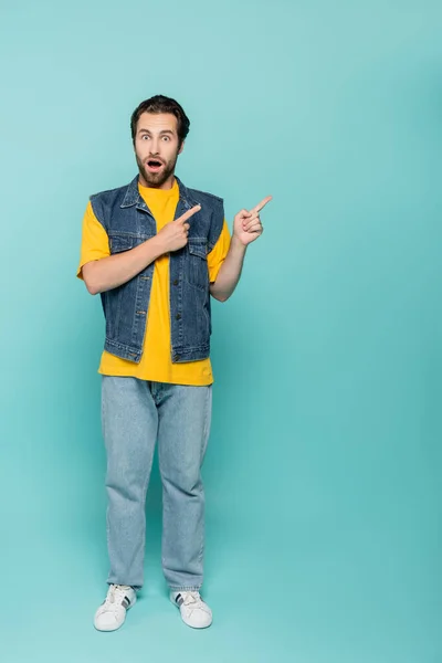 Amazed man in denim vest pointing with fingers on blue background — Stock Photo