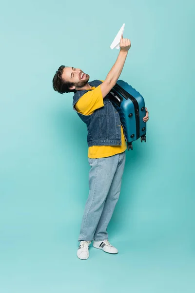 Laughing man holding suitcase and paper plane on blue background — Stock Photo