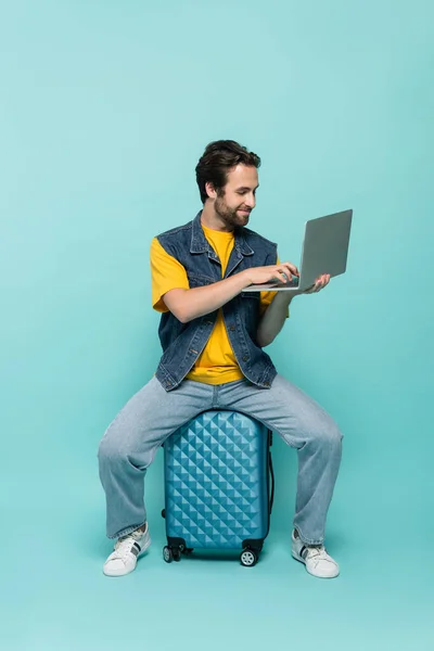 Усміхнений фрілансер використовує ноутбук на валізі на синьому фоні — стокове фото