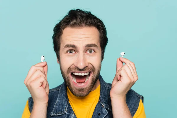 Excited man holding earphones and looking at camera isolated on blue — Stock Photo