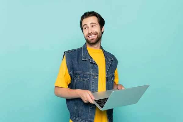 Freelancer sonriente con portátil mirando hacia otro lado aislado en azul - foto de stock