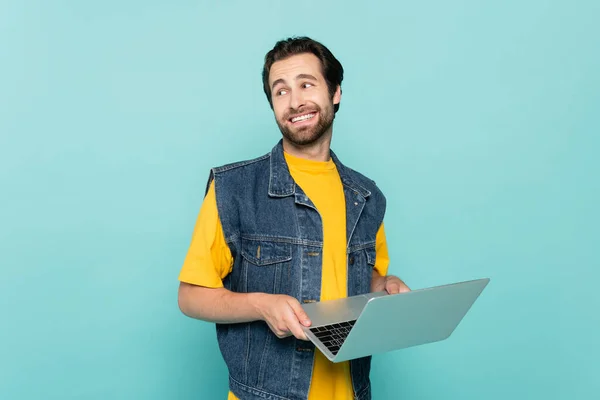 Lächelnder Freiberufler mit Laptop schaut vereinzelt auf blauem Grund weg — Stockfoto