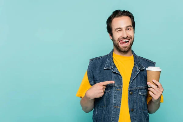 Giovane uomo sporgente lingua mentre indica il caffè per andare isolato su blu — Foto stock