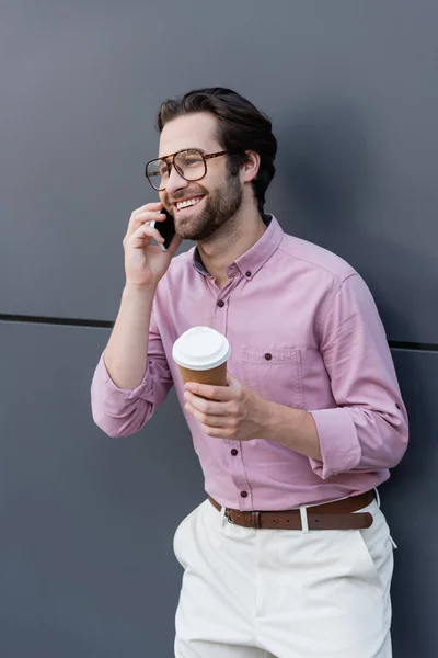 Businessman talking on smartphone and holding coffee to go near building — Stock Photo