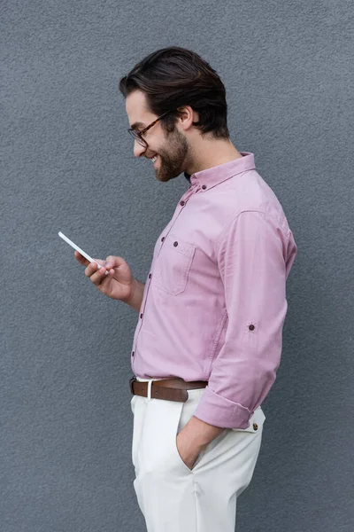 Side view of smiling businessman using smartphone near wall outdoors — Stock Photo