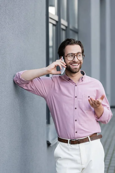 Happy manager in formal wear talking on mobile phone near building — Stock Photo