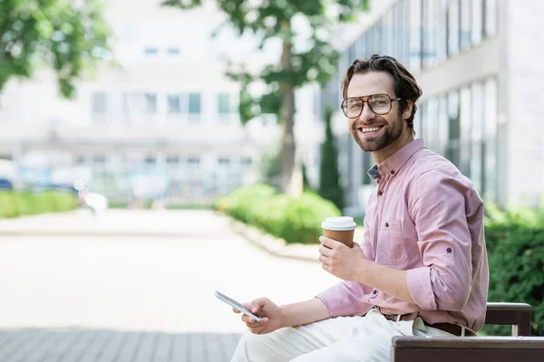 Manager sorridente con drink da asporto e smartphone in panchina all'aperto — Foto stock