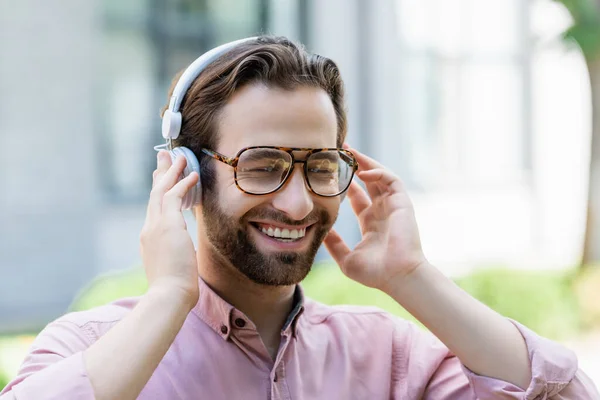 Allegro uomo d'affari in occhiali usando le cuffie all'aperto — Foto stock