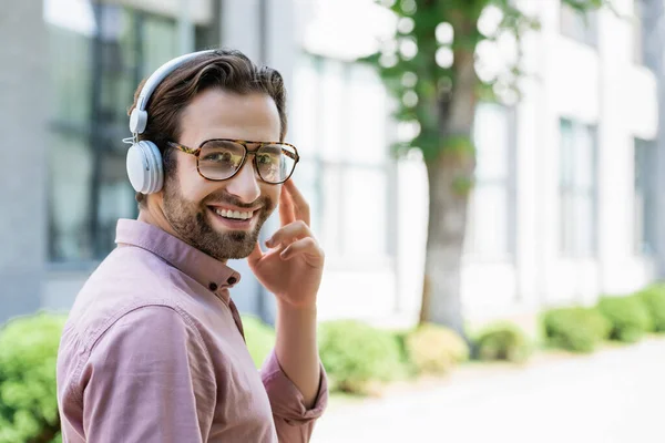 Hombre de negocios sonriente en gafas y auriculares mirando a la cámara al aire libre - foto de stock