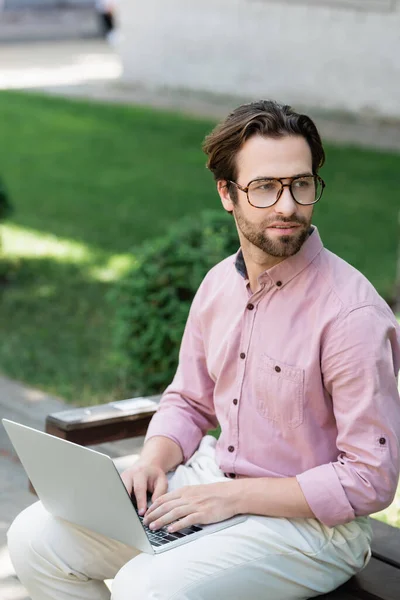 Businessman in eyeglasses using laptop on bench outdoors — Stock Photo