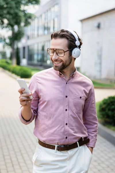 Positive businessman in headphones using smartphone on urban street — Stock Photo
