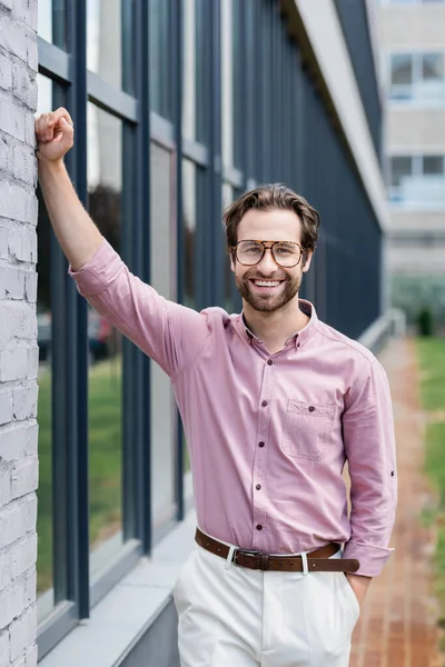 Empresário sorridente em óculos e camisa de pé perto do edifício — Fotografia de Stock