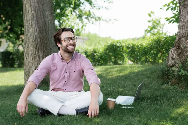 Homme d'affaires heureux assis près des appareils et tasse de papier sur l'herbe — Photo de stock