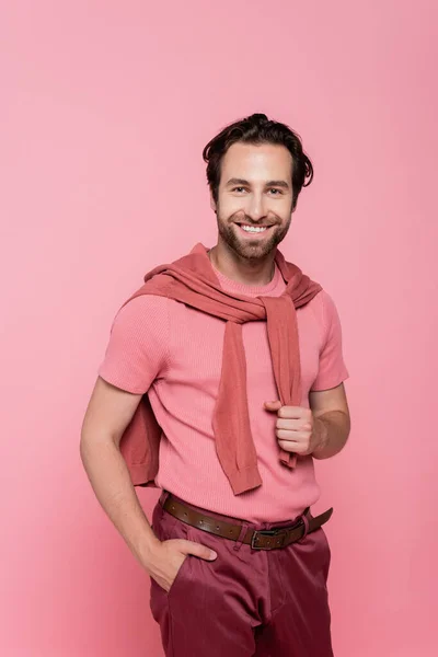 Hombre sonriente sosteniendo la mano en el bolsillo de los pantalones aislados en rosa - foto de stock