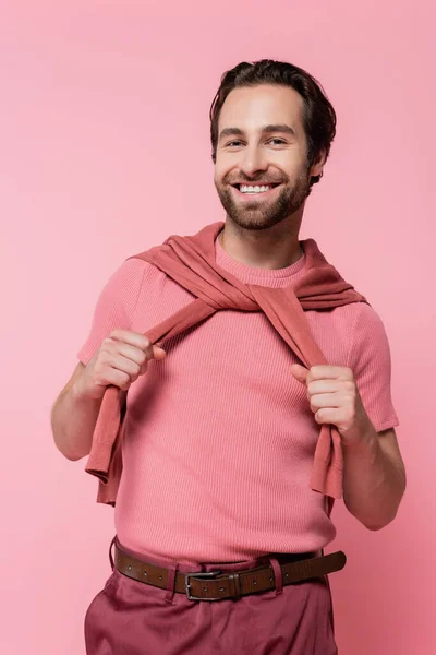 Allegro uomo che tiene il maglione sulle spalle isolato su rosa — Foto stock