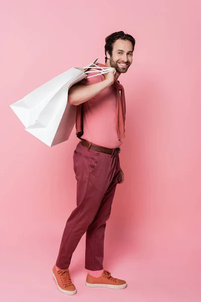 Pleine longueur de jeune homme avec des sacs à provisions en regardant la caméra sur fond rose — Photo de stock