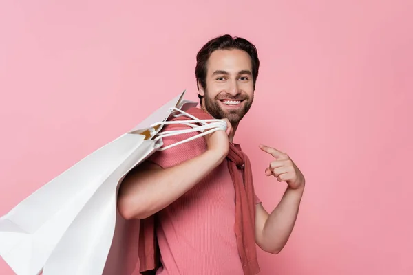 Positive man pointing at shopping bags isolated on pink — Stock Photo