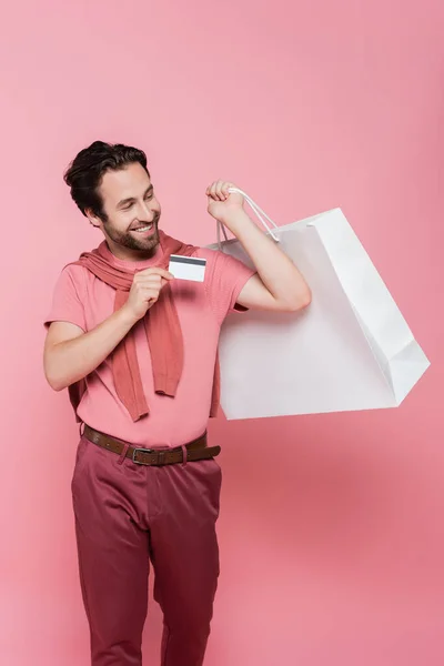 Brunette shopaholic holding shopping bag and credit card on pink background — Stock Photo