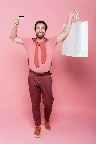 Homem animado com cartão de crédito e saco de compras em fundo rosa — Fotografia de Stock