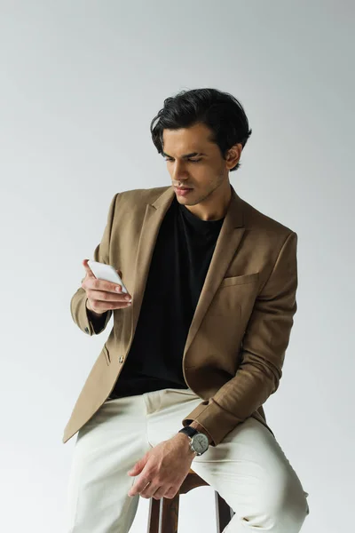 Young man in blazer messaging on smartphone isolated on grey — Stock Photo