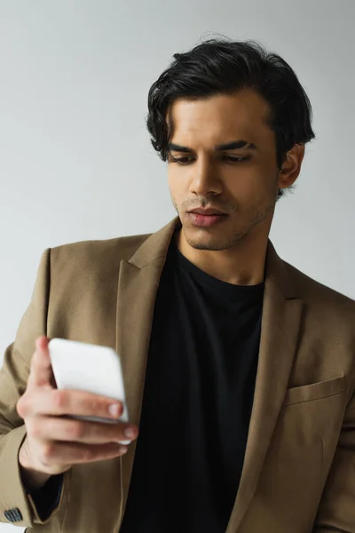 Young man in blazer texting on smartphone isolated on grey — Stock Photo