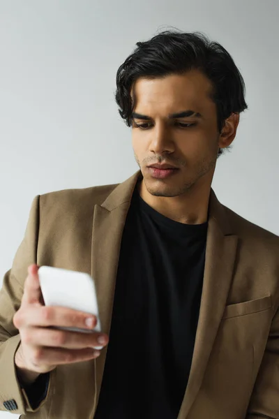 Joven en blazer mensajes de texto en el teléfono inteligente aislado en gris - foto de stock