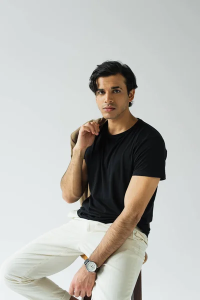 Young man holding blazer while sitting on chair isolated on grey — Stock Photo