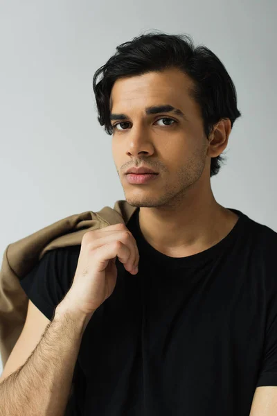 Portrait of young man in black t-shirt holding blazer isolated on grey — Stock Photo