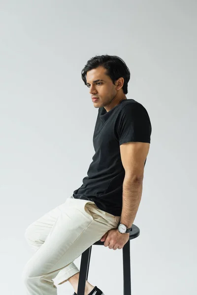 Pensive young man in black t-shirt sitting on chair isolated on grey — Stock Photo