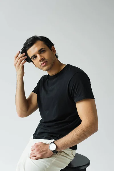 Portrait of young man looking at camera while adjusting hair isolated on grey — Stock Photo