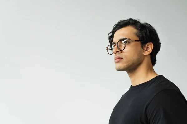 Hombre con estilo en gafas de vista mirando hacia otro lado aislado en gris - foto de stock