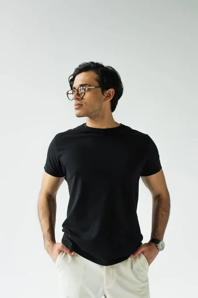 Стильний чоловік в окулярах стоїть руками в кишенях ізольований на сірому — стокове фото
