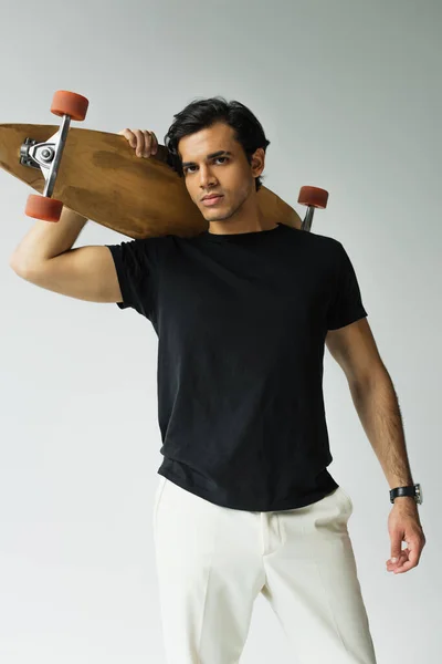 Young man in black t-shirt holding longboard isolated on grey — Stock Photo